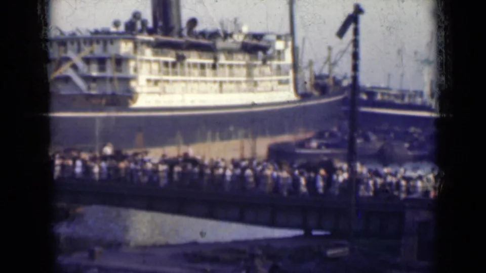 1947 India dock scene with a passenger ship, crowded pier, water, and harbor structures visible through soft 8mm film.