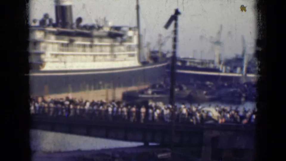 Distant 8mm view of a crowded Indian dock in 1947, with a large ship hull and busy pier activity.