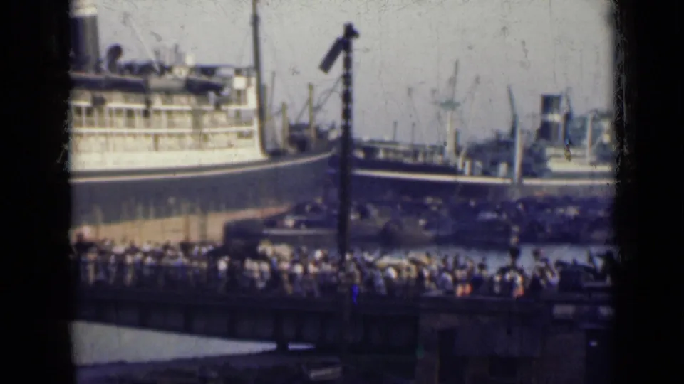 1947 India harbor frame showing a passenger ship at the pier and a dense crowd gathered along the dockside.