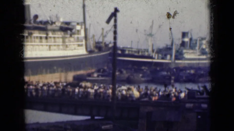 1947 India home-movie frame showing a busy harbor with large vessels, cranes, and a crowd gathered near the waterfront.