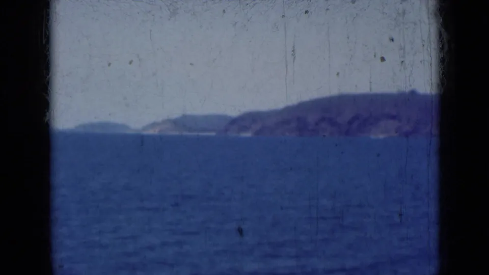 The view shifts from harbor activity to open blue water and a hazy mountainous coastline, consistent with a moving vessel perspective in India.