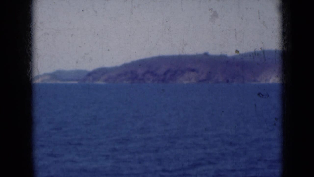 Blue ocean with a distant hazy mountain coastline under a pale sky, framed by dark film edges.