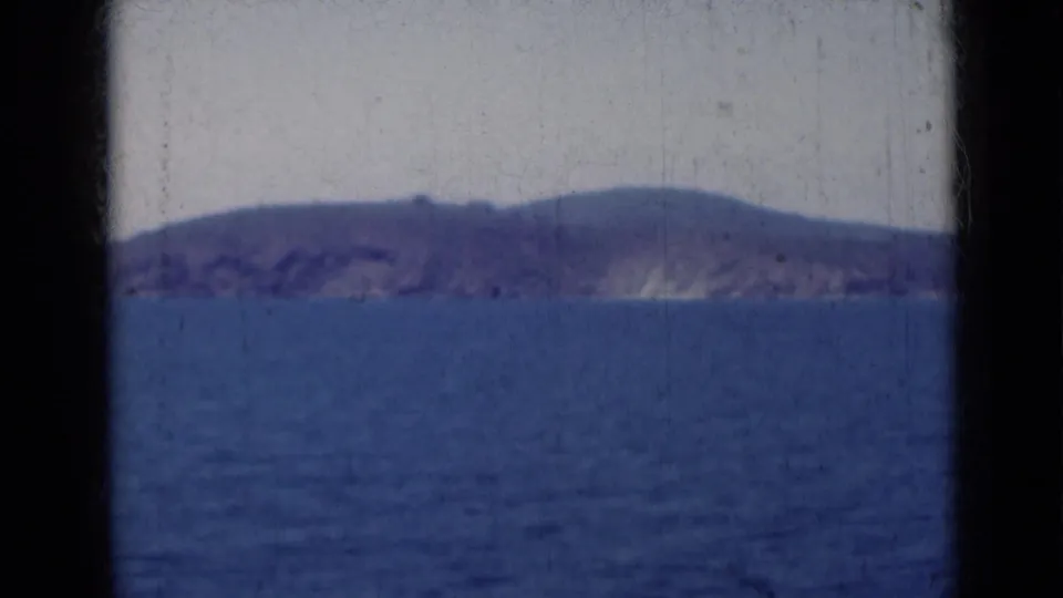 Mid-century 8mm view from India showing a distant hilly shoreline across the ocean, with visible grain and dark frame edges.