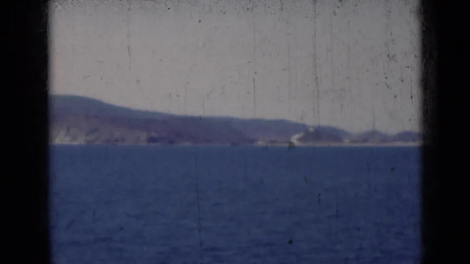 1947 India 8mm frame of blue water facing a distant shoreline with a pale curved feature along the coast.