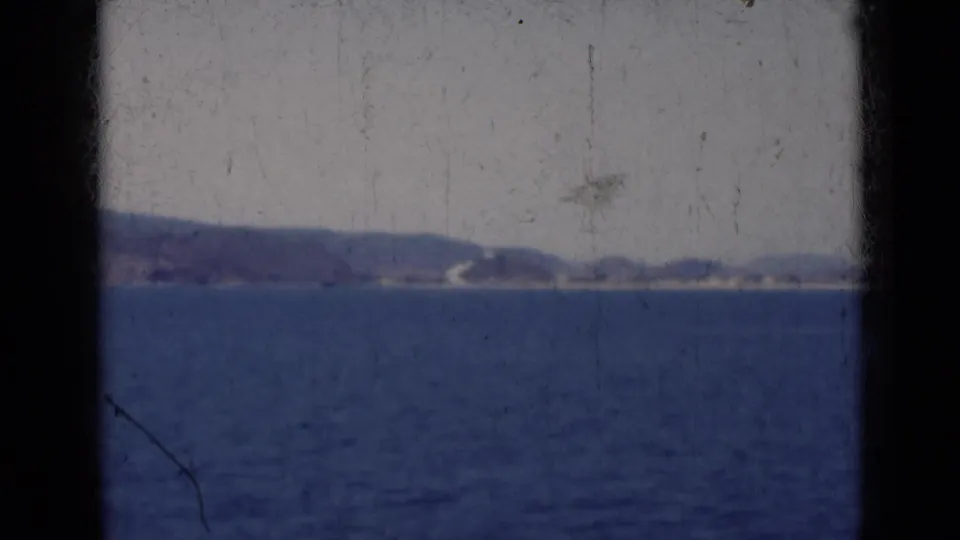 Soft 8mm view of an Indian coastline in 1947, with blue water in front and hazy hills along the horizon.