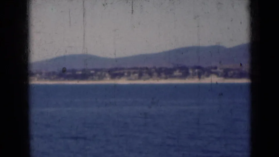 1947 India 8mm frame with calm water in the foreground and a hazy mountain-backed shoreline beyond dark framing bars.
