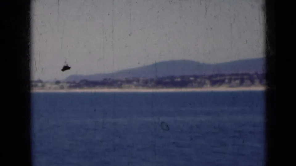 1947 India 8mm frame of calm water and a distant mountain shoreline, with aged-film marks and dark edge framing visible.