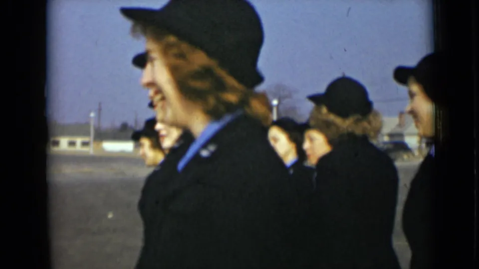 The camera catches a side view as uniformed young women turn and move past on a suburban New York road.