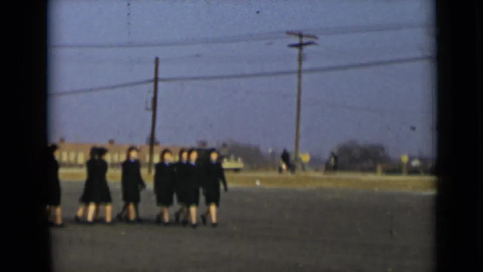 Uniformed women march away in a loose formation under utility wires in 1947 New York home-movie footage.