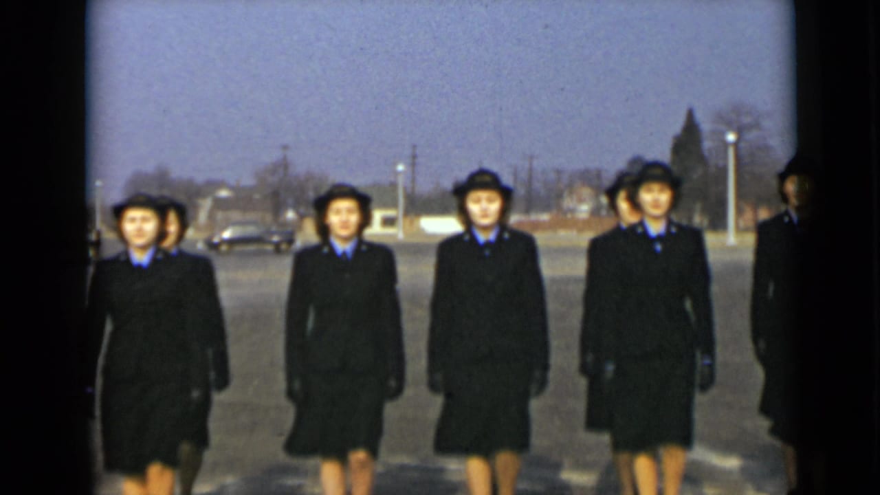 Women in matching dark uniforms and hats approach the camera in a New York 1947 outdoor drill scene.