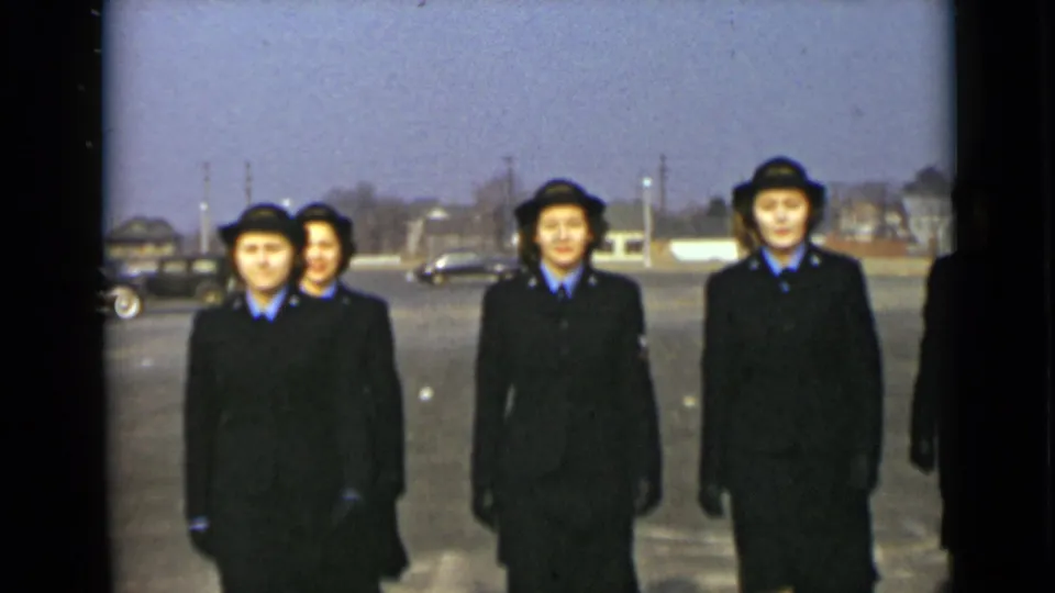 Closer 8mm view of women in dark coats, hats, and blue collars marching in formation in 1947 New York.