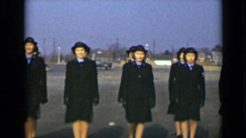 Four uniformed women in dark coats and hats walk toward the camera in 1947 New York home-movie footage.