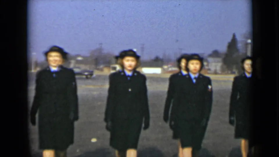 In 1947 New York footage, uniformed women in dark coats, hats, gloves, and blue collars march toward the camera on a paved lot.