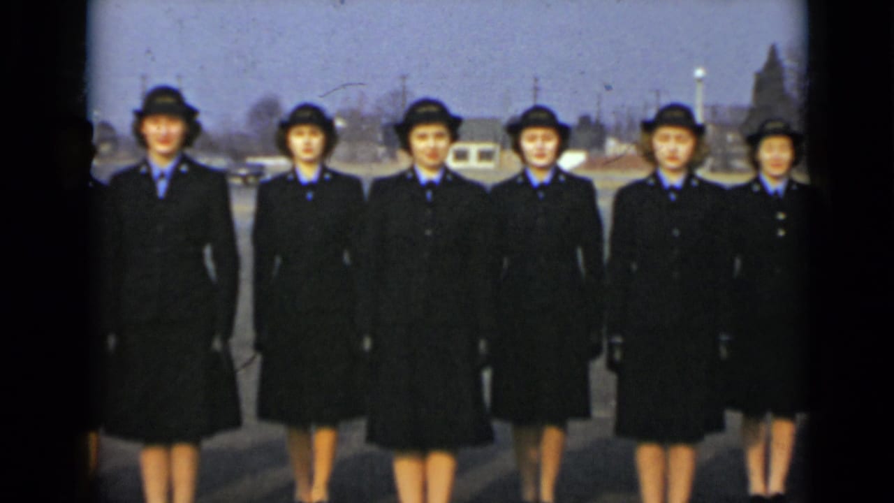 Six women in matching dark uniforms face the camera in an outdoor New York setting, with parked vehicles and utility poles in the background.