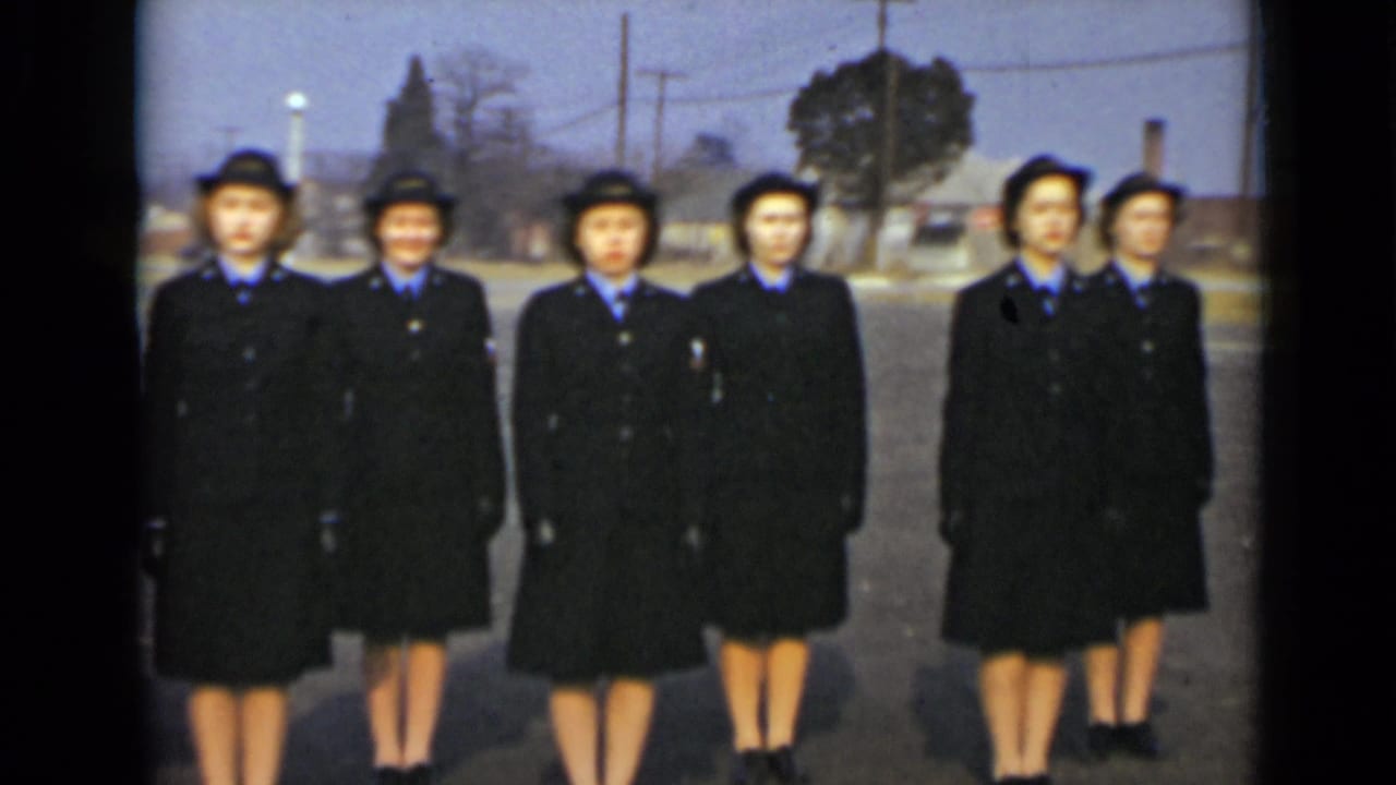 Women in matching blue military-style uniforms stand together outdoors in New York, with utility poles and buildings behind them.