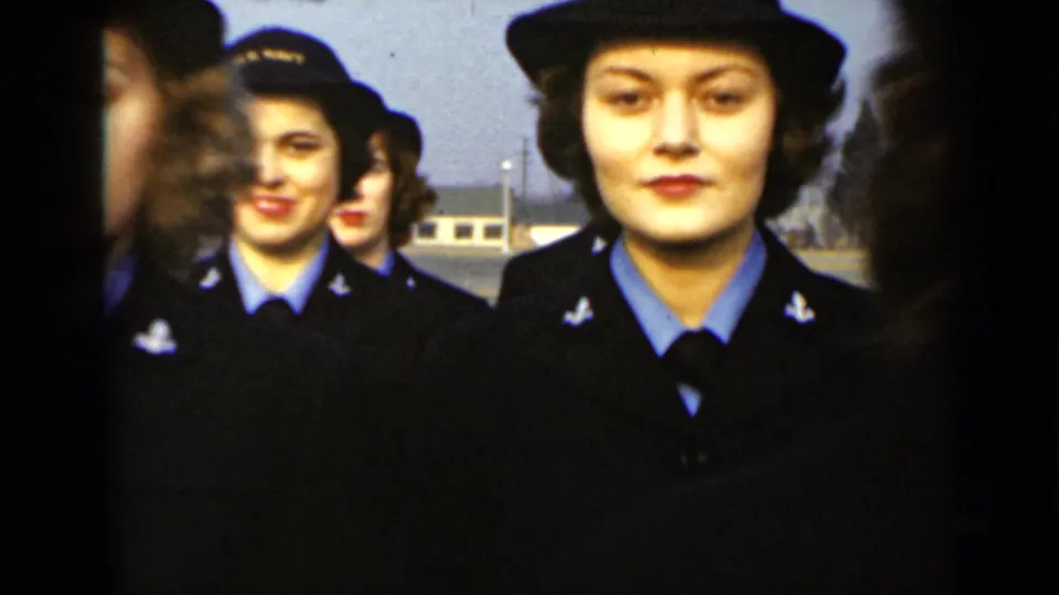 Centered 1947 New York frame of a woman in a dark military-style uniform and hat, with other uniformed women aligned behind her.