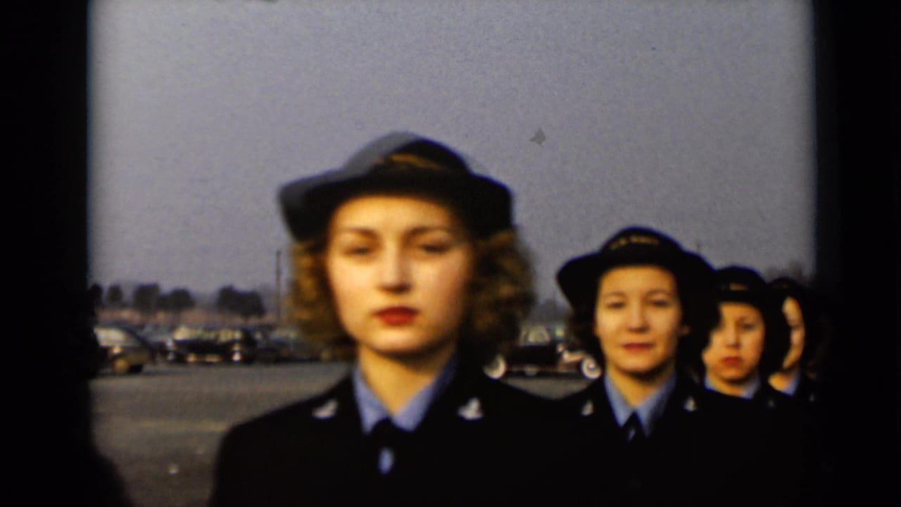 A line of uniformed women faces forward while marching outdoors.