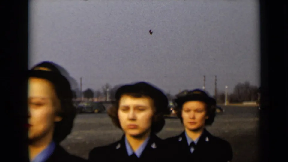 Late moment in the 1947 New York clip showing uniformed women continuing past the camera with cars and trees behind them.