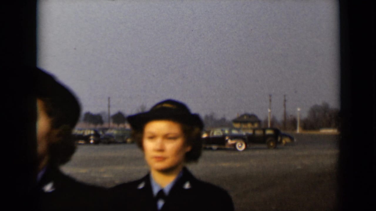 Two women in dark Navy-style uniforms stand in a paved lot with parked cars behind them.