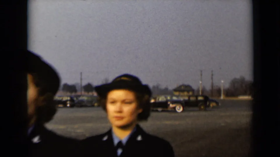 1947 New York home-movie frame showing women in U.S. Navy-style uniforms posing in a parking lot with period cars in the distance.