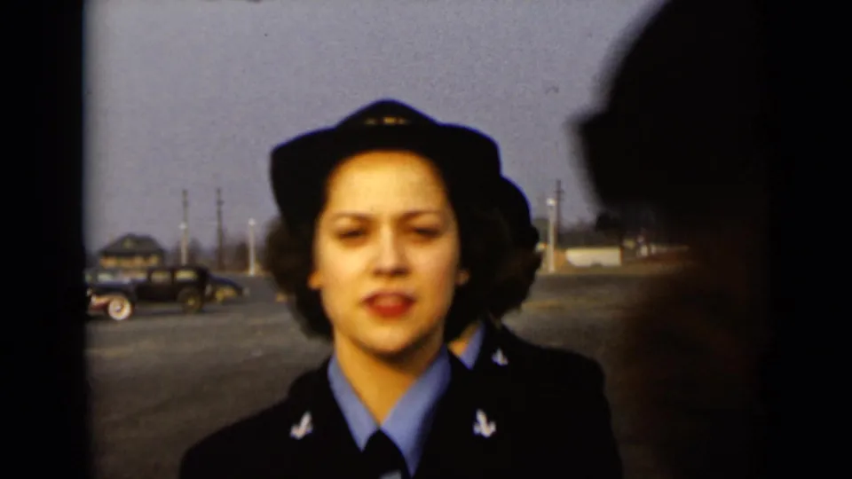A woman in a U.S. Navy cap smiles toward the camera in 1947 New York footage as another figure crosses the foreground.