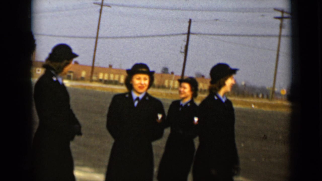 Four women in dark uniforms and hats stand on a paved outdoor area.