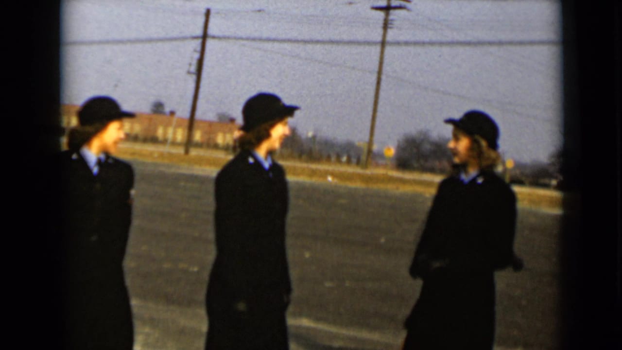 Three uniformed women face each other on a paved field.
