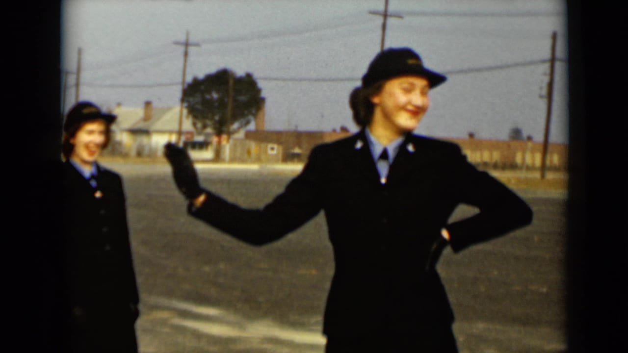 Uniformed women stand on a paved lot as one woman smiles and waves.