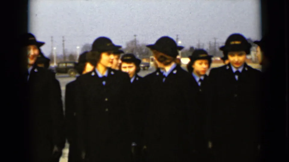 Uniformed women in 1947 New York stand in a loose outdoor line, with houses and utility poles in the background.