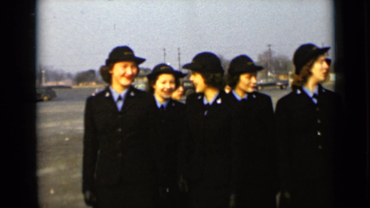 Women in matching dark uniforms smile and look toward one another outdoors.