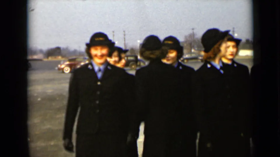 A woman in a dark uniform and hat smiles near the front of the group as others stand behind her in the New York parking lot.