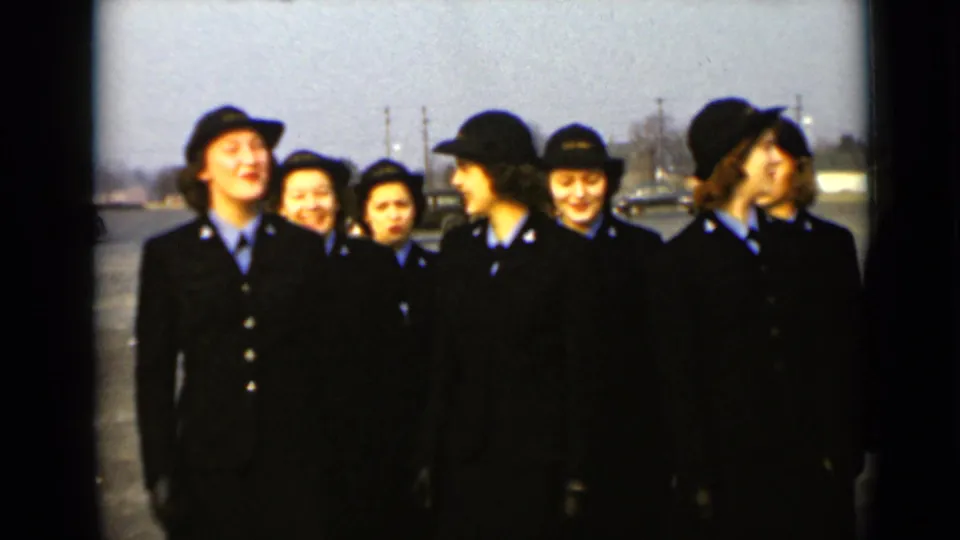 The group of uniformed women remains loosely gathered in 1947 New York, with faces visible and cars in the background.