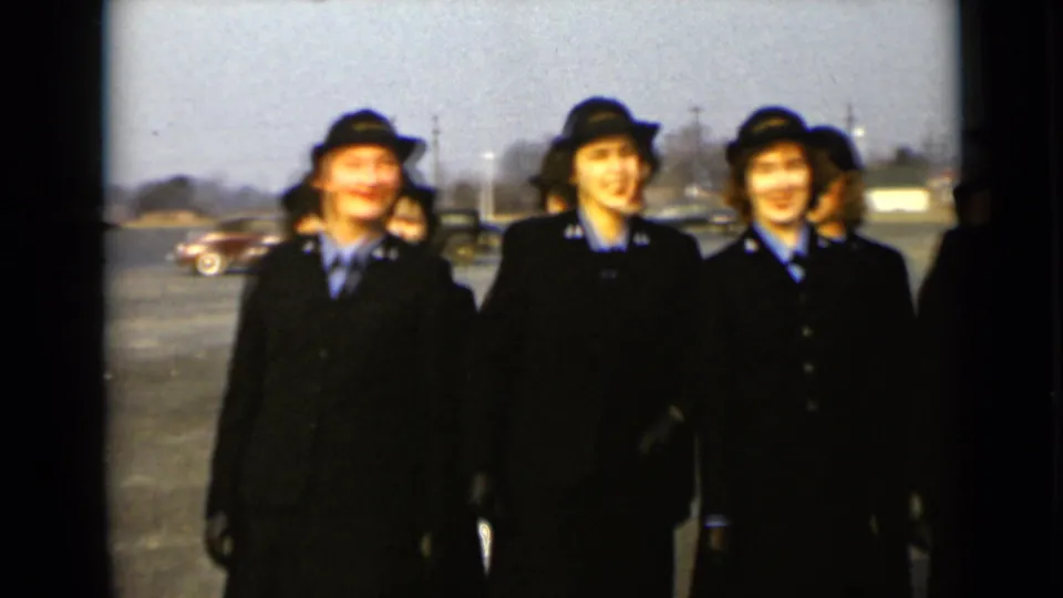Three women in matching dark formal uniforms and hats stand outdoors in 1947 New York, with cars and low buildings in the distance.