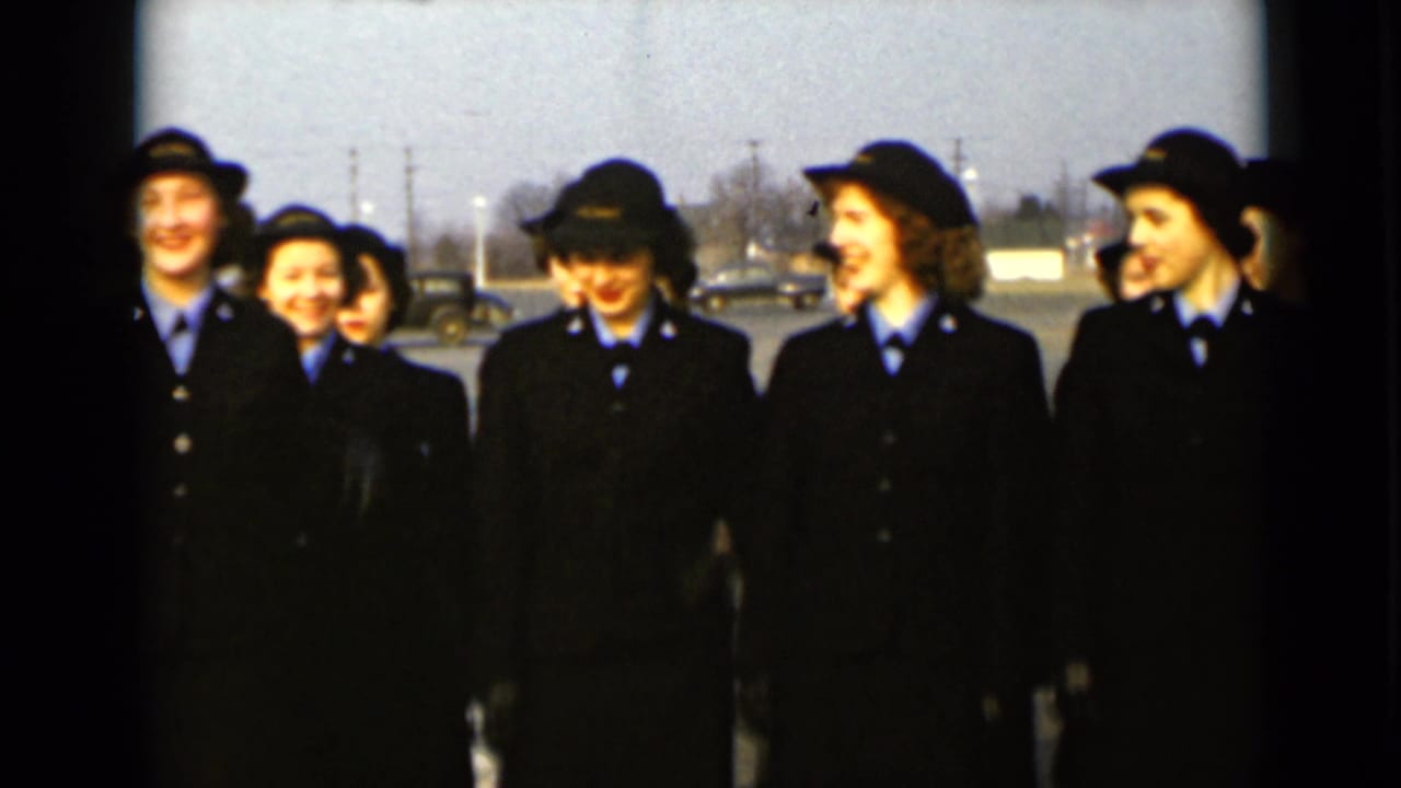 A group of uniformed women smile and turn toward each other outdoors.
