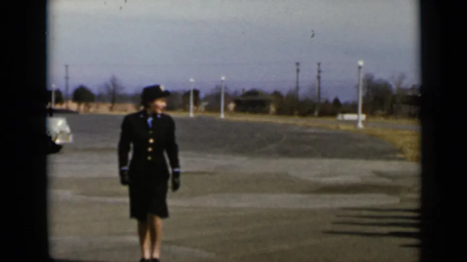 A woman in a dark uniform-style suit and hat stands on a paved lot in New York archival footage from 1947.