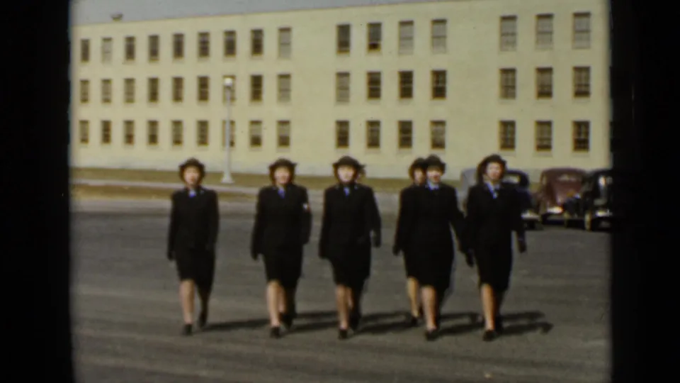 Five women in dark uniform-style suits walk in formation before a large institutional building in 1947 New York footage.