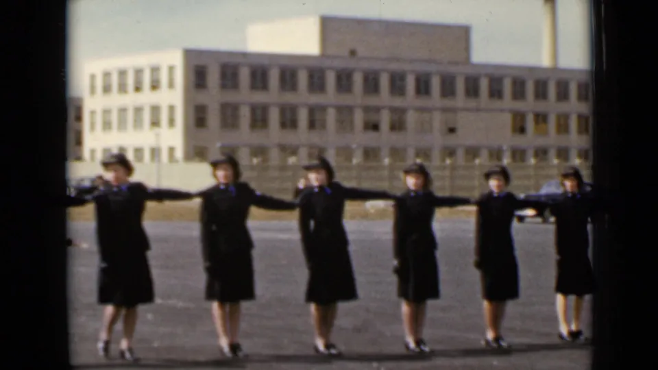 In 1947 New York footage, uniformed women extend their arms in a spacing drill before a large institutional building.