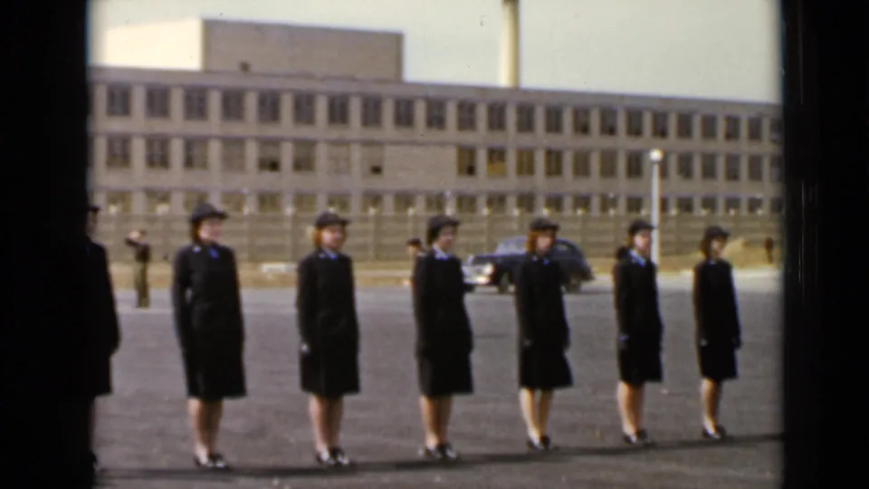At the end of the 1947 New York clip, the uniformed women stand aligned on the paved lot near a building and parked car.
