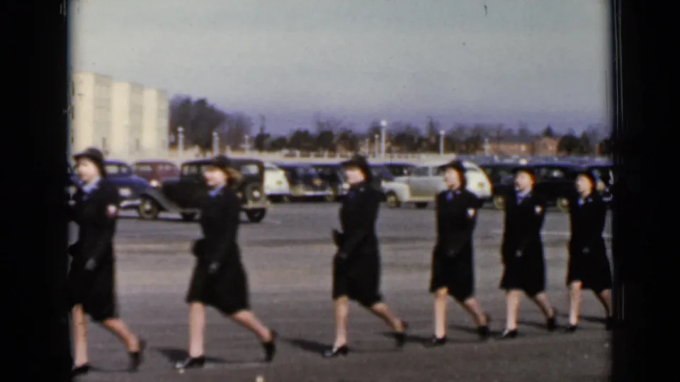 A closer 1947 New York frame shows uniformed women marching past the camera, with parked cars and buildings behind them.