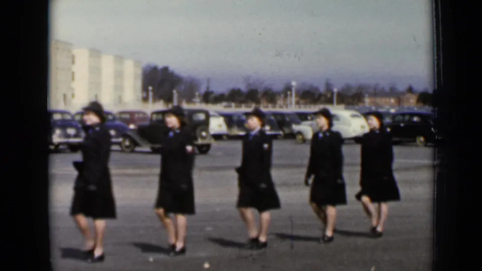The final frame keeps the marching women centered against rows of 1940s cars and a pale building in New York.
