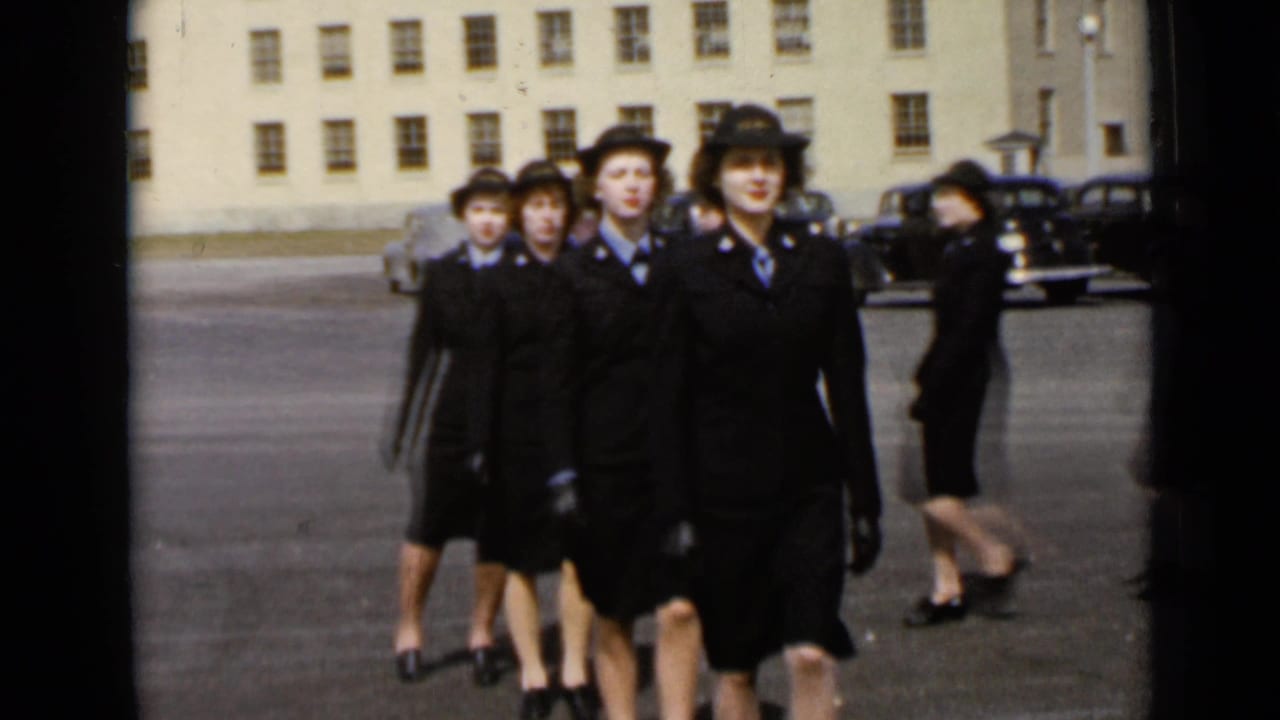 Uniformed women march toward the camera across a paved courtyard.