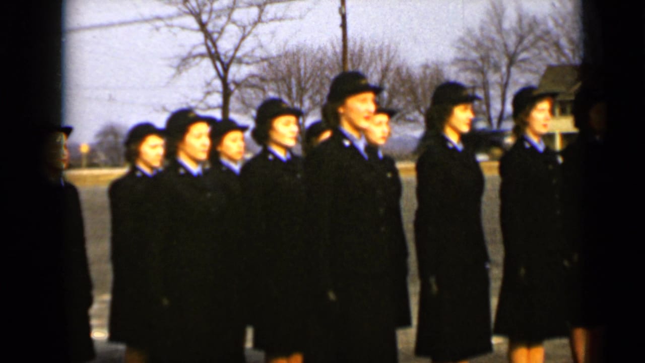 Uniformed women in dark coats and hats stand in formation on a quiet street.