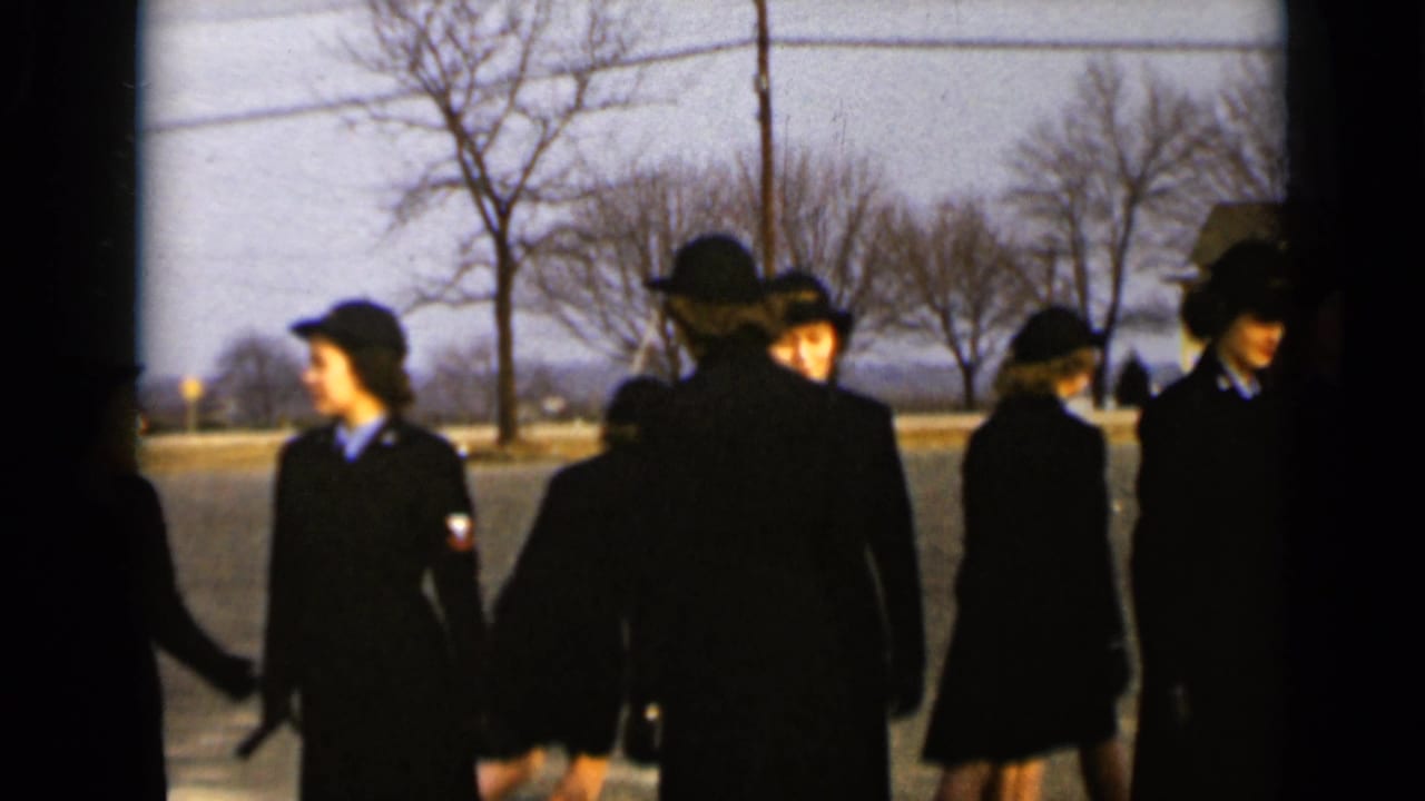 Women in matching dark uniforms turn and move out of formation near bare trees.