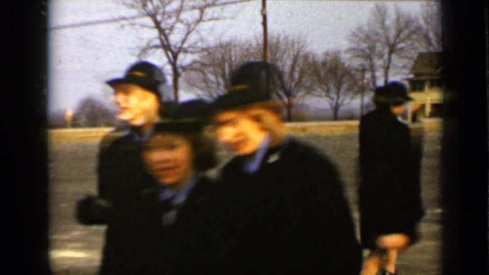 Soft, blurred 8mm frame of uniformed women in dark coats near the camera on a New York street, with another woman walking behind them.