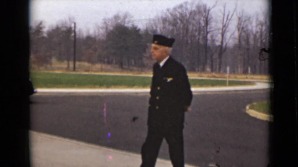 The uniformed man walks along the roadside in the 1947 New York home-movie scene, with grass and leafless trees behind him.