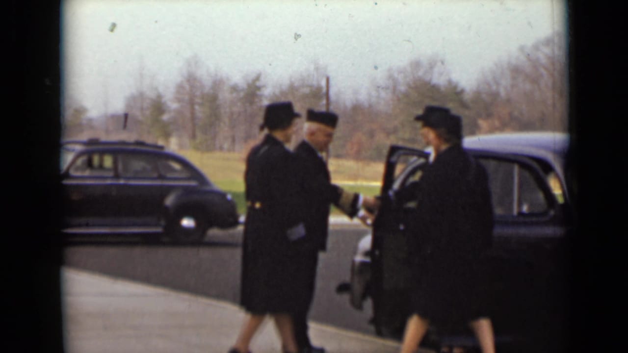Two women and a uniformed man stand by an open car door.