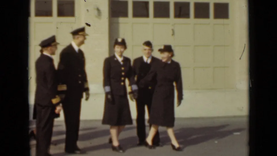 Uniformed men and women gather outside large bay doors in 1947 New York, with faces and dark formal uniforms visible.