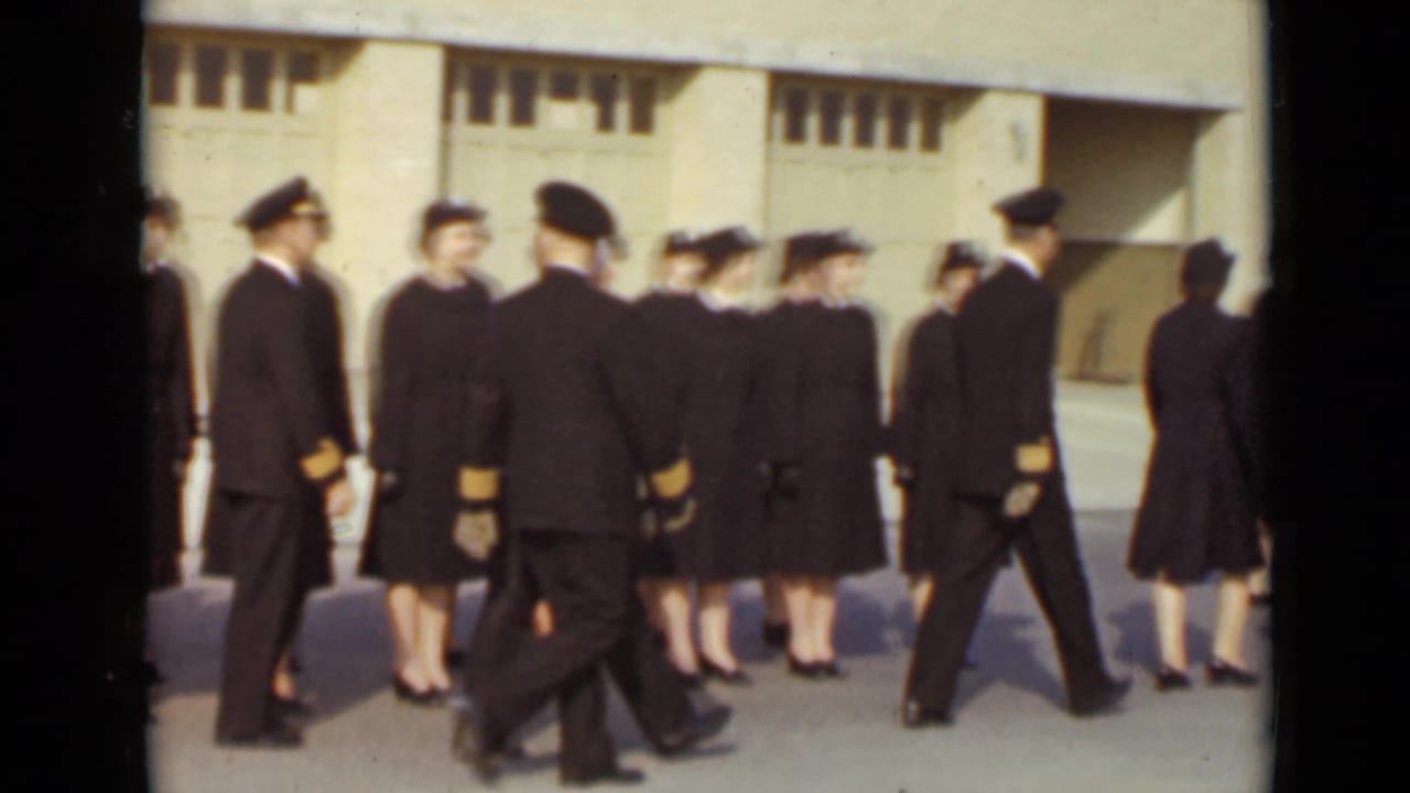 A uniformed group marches past the building in close formation.