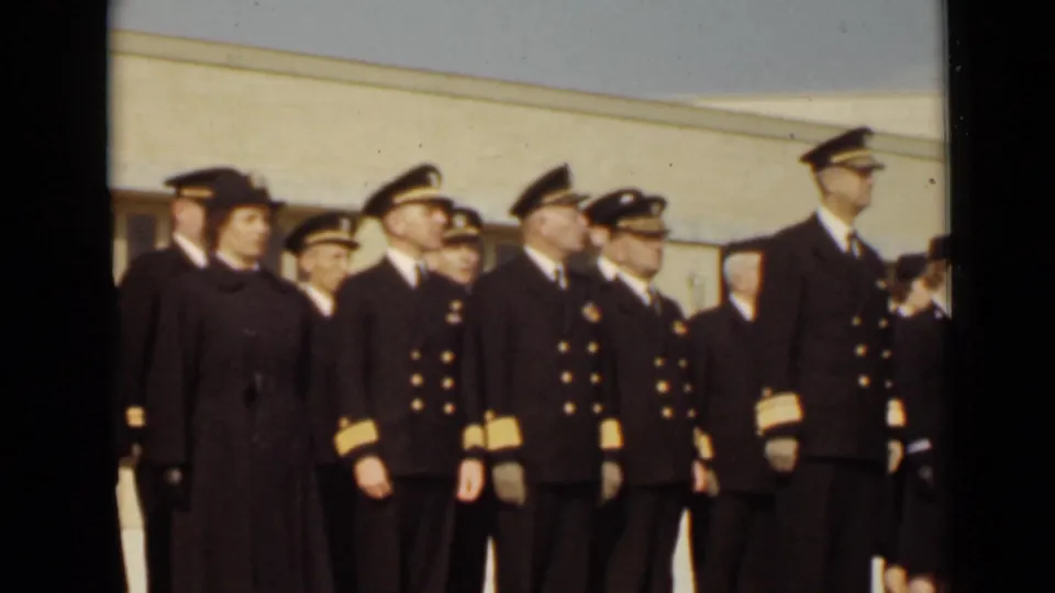 Several male officers in peaked caps and uniformed women stand together outside a light-colored institutional building in 1947 New York.