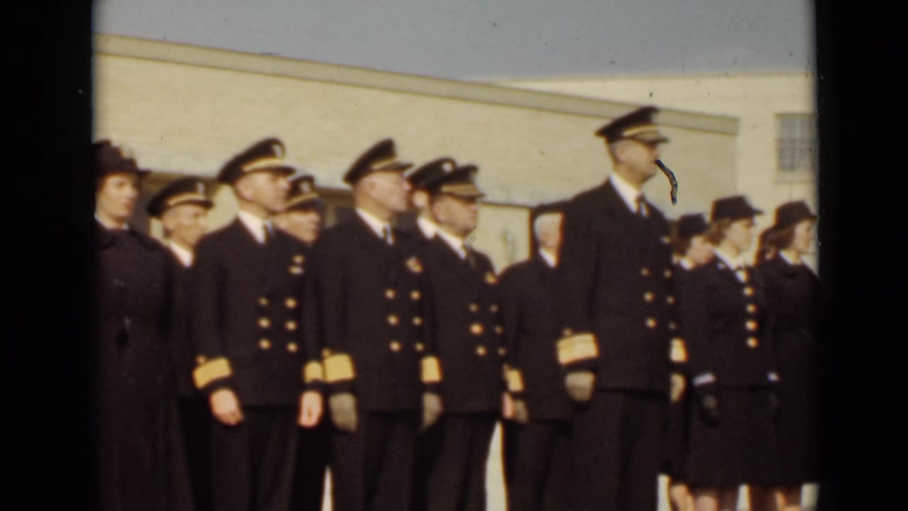 In 1947 New York footage, uniformed sailors and women in service attire stand at attention outdoors beside a plain institutional building.